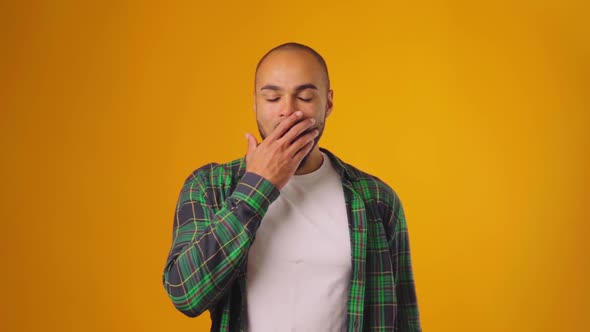 Sleepy Tired African American Man Yawning and Closing Mouth with Hand Against Yellow Background