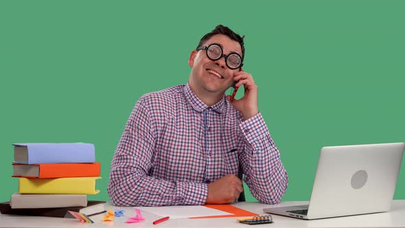 A Man Sits at a Table in Front of an Open Laptop and Talks on a Cell Phone