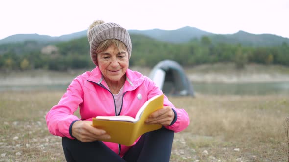 Authentic Shot of Senior Woman Camping with Tent While Reading a Book Outdoor in a Mountain Lake