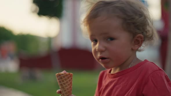 Fairhaired Boy Eats White Cold Cream Ice Cream in Waffle Cone Cup While Sitting Outside in Sunny