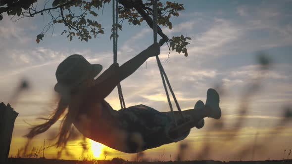 Silhouette Young Girl Swinging on a Swing Under a Tree in Sun. Family Fun in Nature