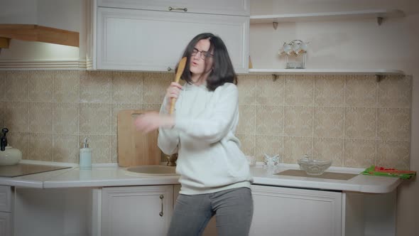 Girl is Having Fun Dancing and Singing on the Background of the Kitchen Holding a Spoon and Singing