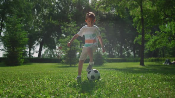 Young Boy Making Football Exercise on Grass in Park