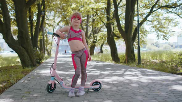 Athletic Fit Young Girl Rides on Electric Scooter Standing Near Bike Looking at Camera in Park