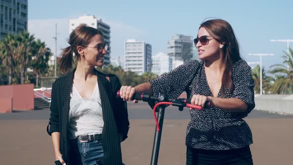 Talking woman walking by friend pushing electric scooter in city