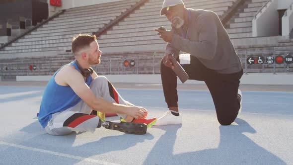 Diverse male coach and disabled athlete with prosthetic leg talking during training session