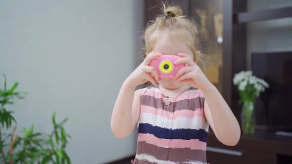 a Funny Little Girl Takes a Photo on a Little Pink Toy Camera