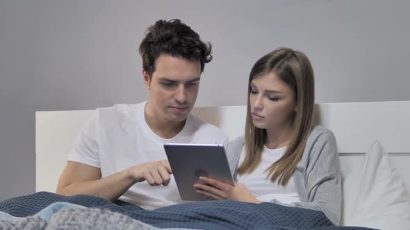 Relaxing Young Couple Browsing Internet on Tablet in Bed