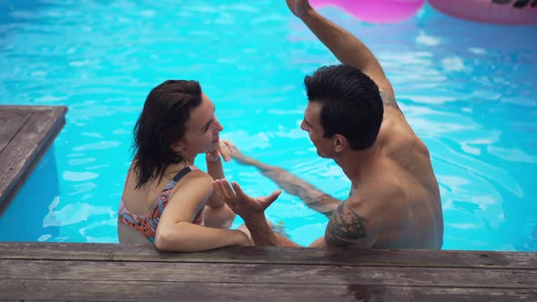 Relaxed Interracial Couple Sitting in Azure Swimming Pool at Resort Talking Laughing in Slow Motion