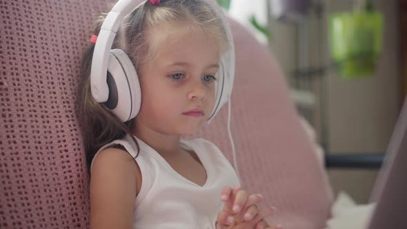 Little Girl Sitting Sofa in Headphones Listen Music Use Laptop Have Fun Home Interior Caucasian