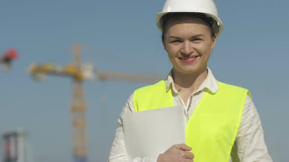 Girl Builder in Protective Clothes at Construction Site. Girl Holds a Folder with Documents and