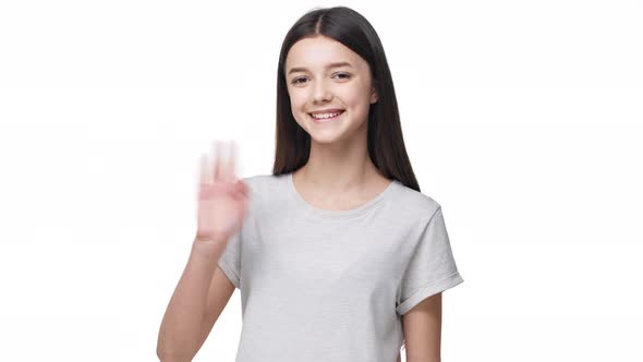 Portrait of Friendly Young Woman with Clean Face Smiling on Camera and Waving Hand with Greeting