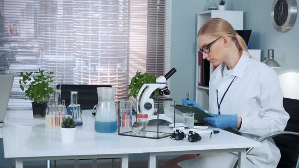 Smart Female Chemistry Scientist in Lab Coat Writing the Results of the Experiment