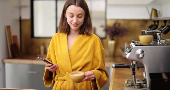 Woman with Coffee and Phone on the Kitchen in the Morning