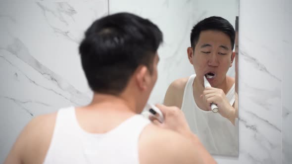 Asian Man Cleaning Teeth Using Electric Toothbrush