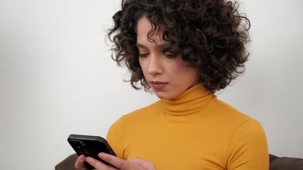 Hispanic Curly Woman Student Uses Smartphone Tapping Screen Display at Home