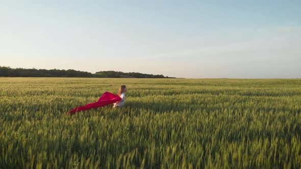 Young Girl Running with Red Tissue in Green Field