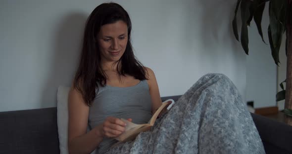 Young Woman at Home Sitting on Sofa Relaxing in Her Living Room Reading Book