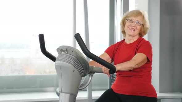 Portrait of Active Old Female Person in Gym Doing Cardio Training on a Exercise Bike