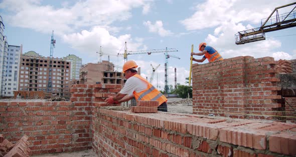 Male Worker Lays Brick Into Wall with Cement Using Trowel