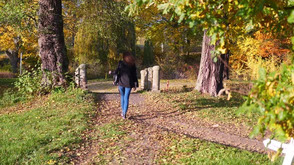 Slow Motion of Young Woman in Casual Outfit With a Bag Walking at Park in Autumn Leaves Colors on Su