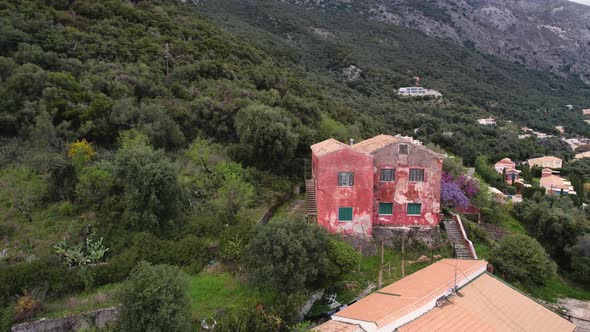 Counter clockwise rotating shot of red, old house in the forest covered mountains of Corfu. Revealin