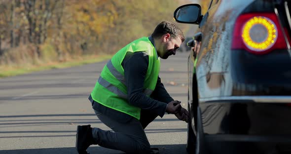 Businessman Changing a Car Wheel on a Road in Sunny Day