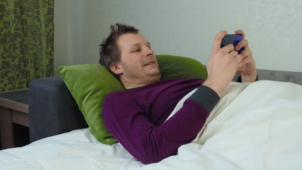 Man Covered with a Blanket Is Lying on the Bed and Playing a Mobile Game. Insomnia Concept