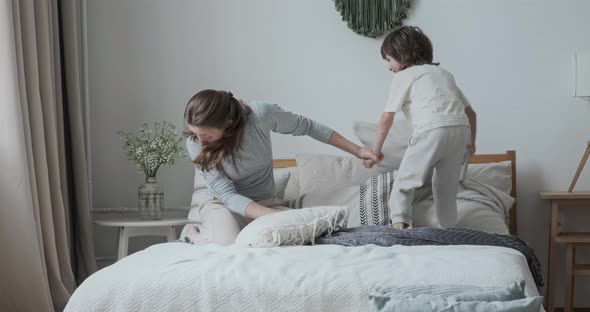 Laughing Mom Fooling Playing with Cute Child Son Lying Jumping on Comfy Bed at Bedroom