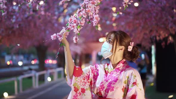 woman in yukata (kimono dress) wear a face mask and looking sakura flower or cherry blossom blooming