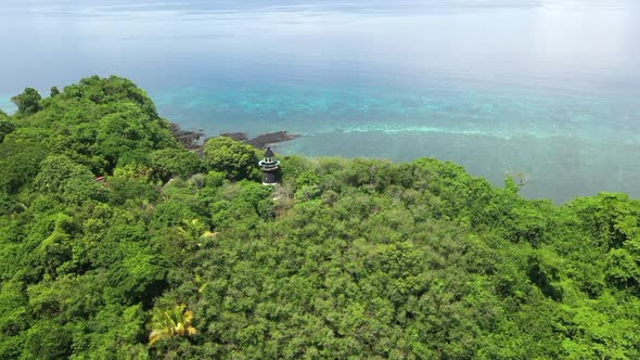 Rotating aerial shot of a lighthouse on a tree covered mountain on an island off Madagascar