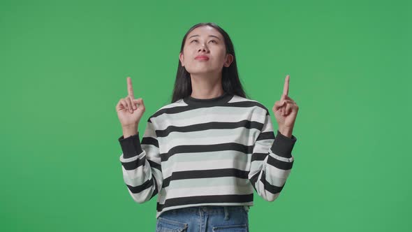 Asian Woman Pointing Up While Standing In Front Of Green Screen Background