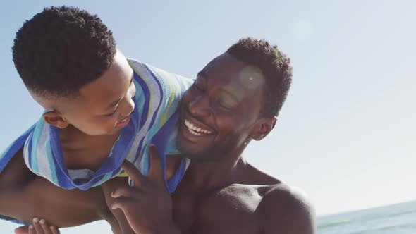 Portrait of smiling african american father carrying his son on sunny beach
