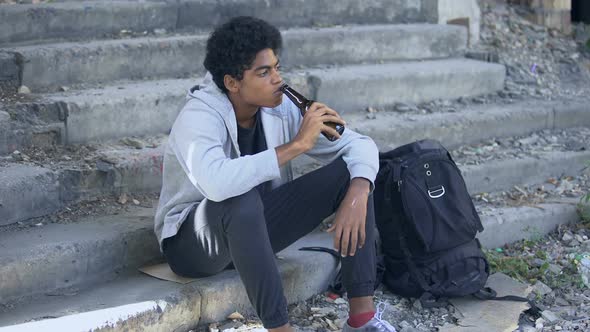 Depressed African Teenager Drinking Beer From Bottle Sitting Stairs, Puberty Age