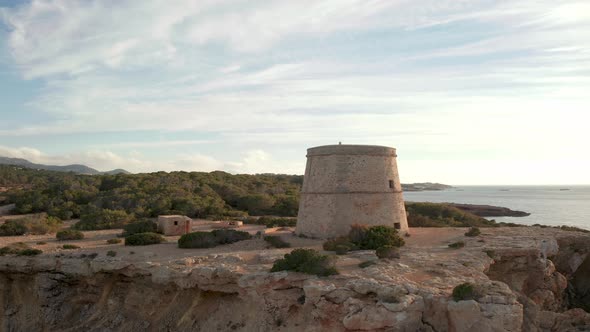 Aearial view of pirate tower in Ibiza. Panning around to show landscape and lookout tower during sun