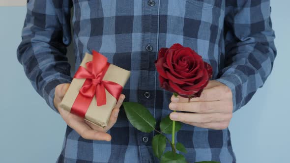 Man holds gift and red rose in hands for Valentine's Day, Birthday or International Women Day