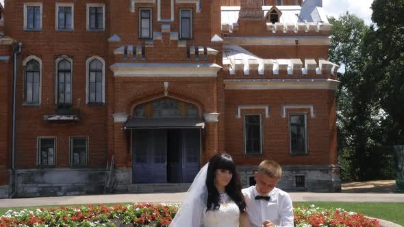 Newlyweds are Sitting Hugging Against the Background of an Old Castle