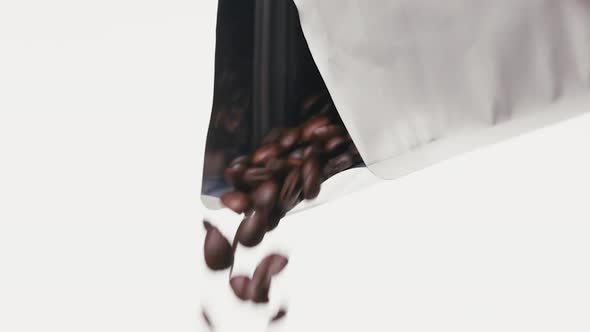 Roasted Coffee Beans Falling Down from Metallic Noname Coffee Bag in Front of White Background. Pour