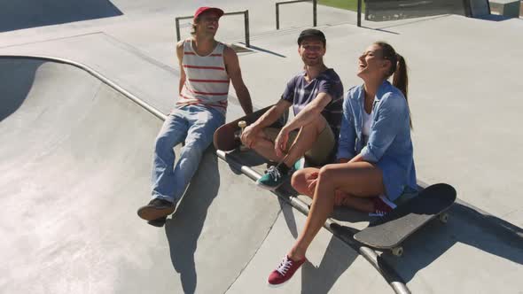 Happy caucasian woman and two male friends sitting, laughing and spending time together on sunny day