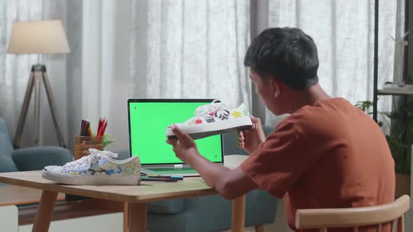 Asian Boy Footwear Designer With Mock-Up Green Screen Laptop Looking At Sneakers