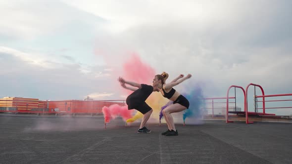 Slow Motion Young Female and Man Doing a Backflip Multi Colored Smoke Bombs on a Background