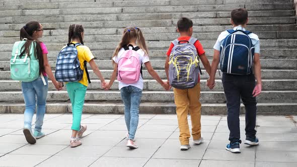 Schoolchildren with Backpacks Go Up Stairs Joining Hands