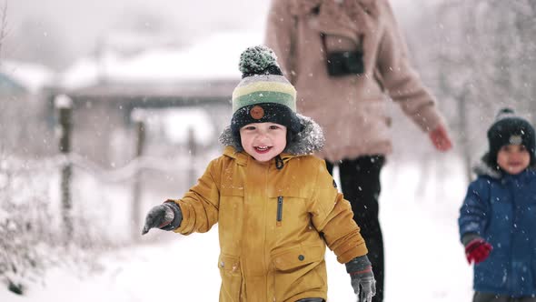 Amazing View of Toddler Boys and Mom Walking in Winter Forest with Snowfall Background