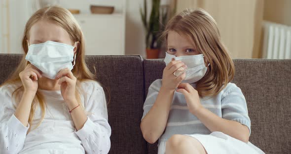 Two Cute Little Little Girls Girlfriends Sister Sitting Together at Home in Room on Couch Wear