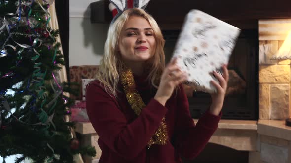 Portrait of Joyful Caucasian Blond Woman Catching Christmas Present and Shaking the Box. Smiling