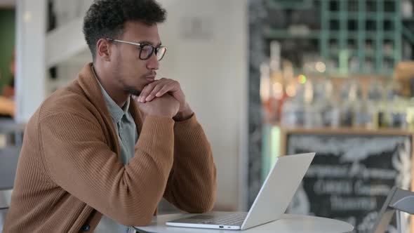 African Man Thinking While Using Laptop in Cafe