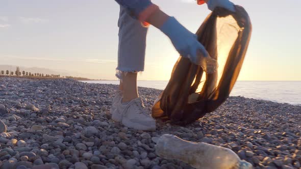 a female volunteer collects garbage in a black garbage bag.