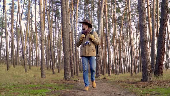 A Man with Camera Walks Along a Trail in the Forest