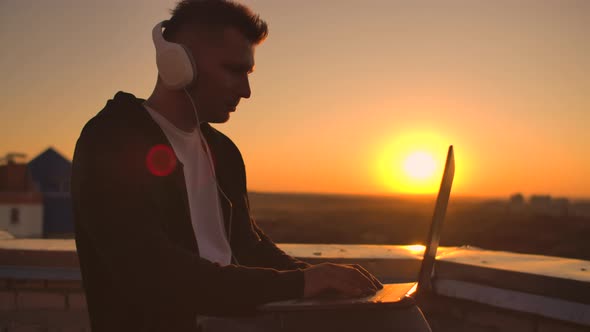 Rear View of a Man in Headphones Listening To Music and Working on the Roof of a Building at Sunset