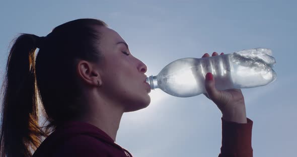 Woman Drinks Water From A Bottle A Close Up Profile Shot With Backlit With Sun And Blue Sky